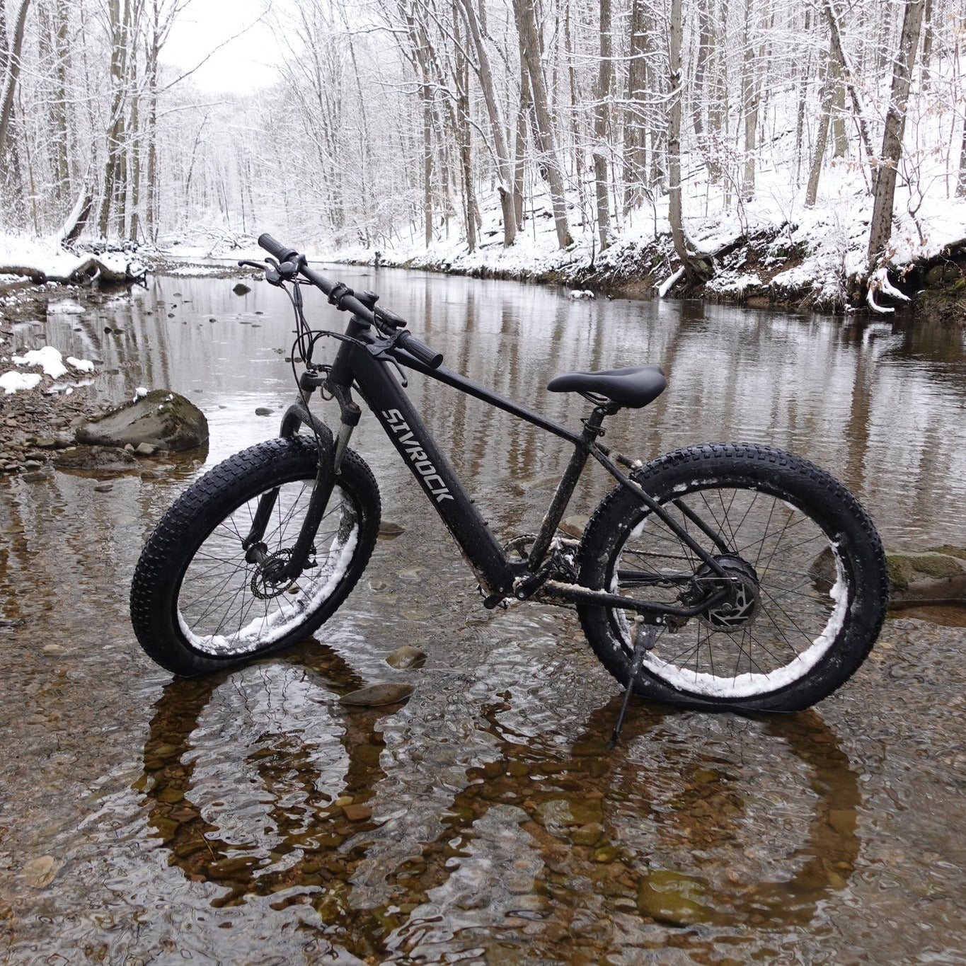 Black electric bike on a snowy forest path with a river in the background